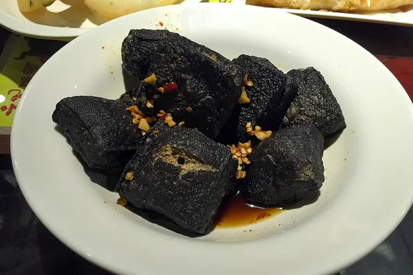 Fried black stinky tofu chunks topped with chili oil and minced garlic on a plate