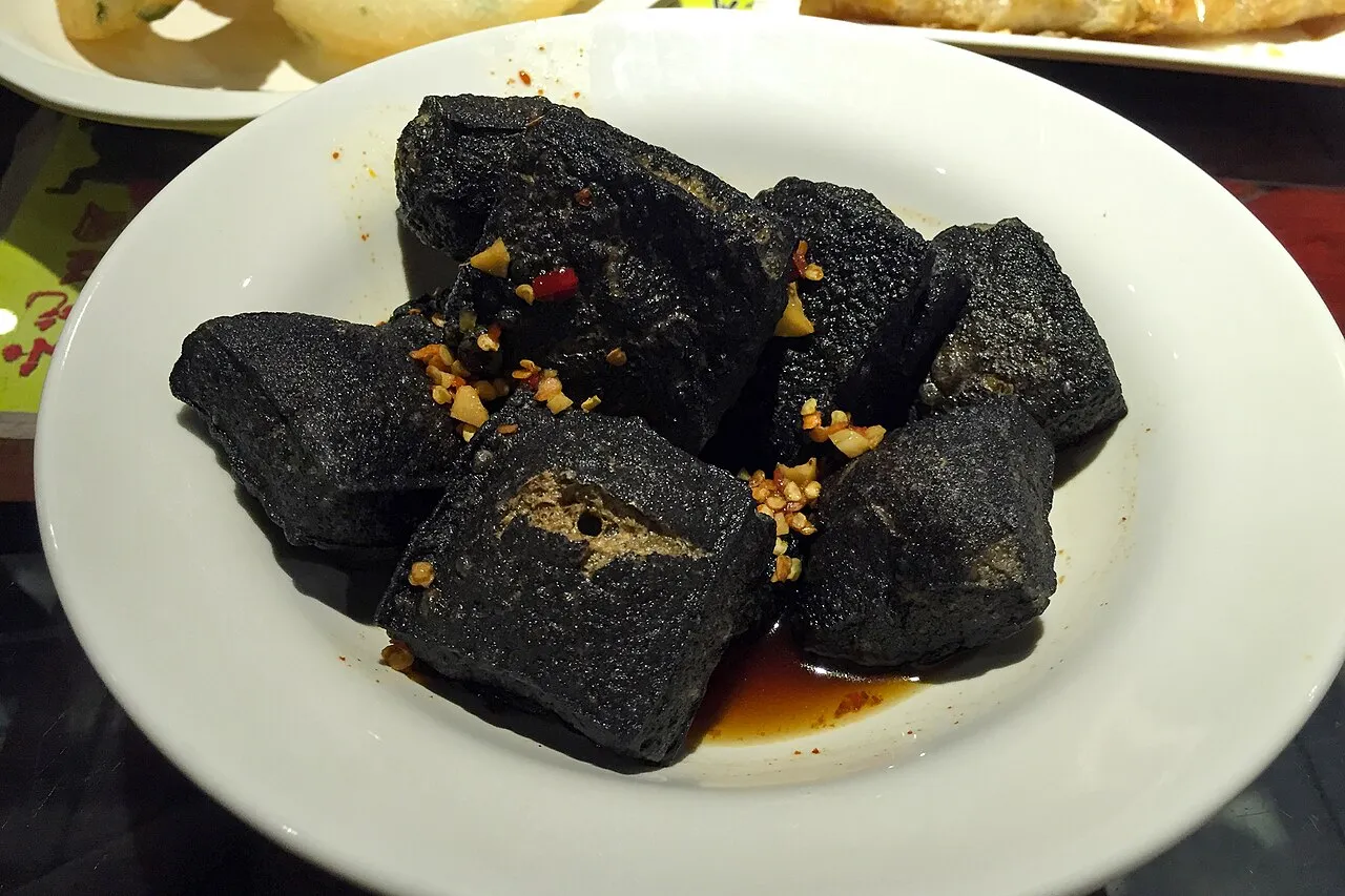 Fried black stinky tofu chunks topped with chili oil and minced garlic on a plate