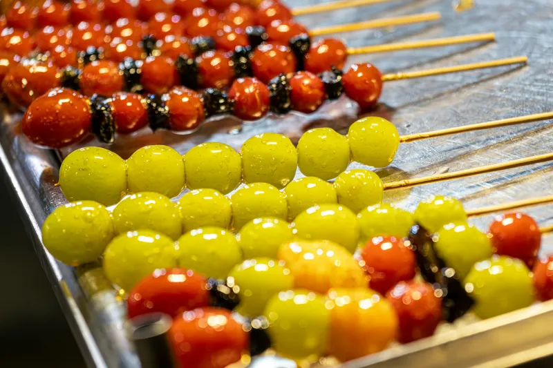 Rows of candied tanghulu skewers — glazed grapes and cherry tomatoes on a stall tray