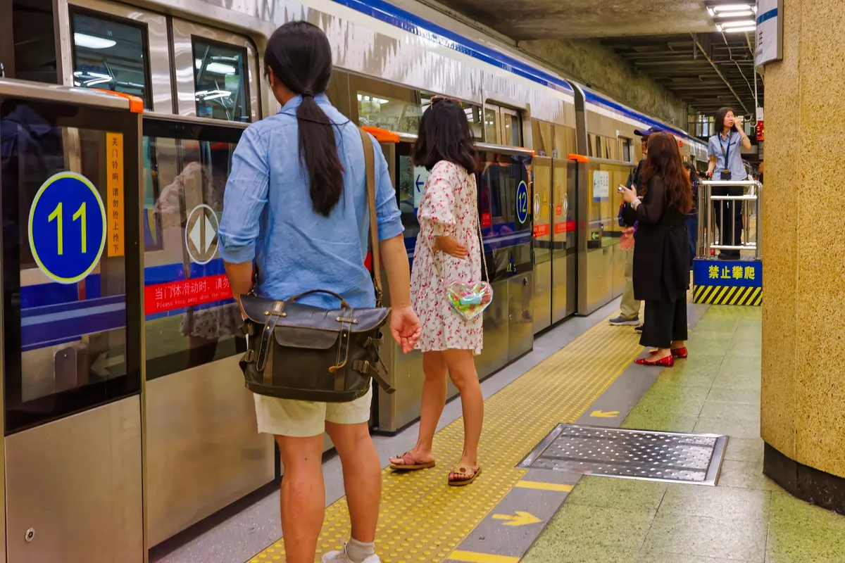 Passengers waiting to board a Beijing subway train at a platform with numbered door markers and safety signage
