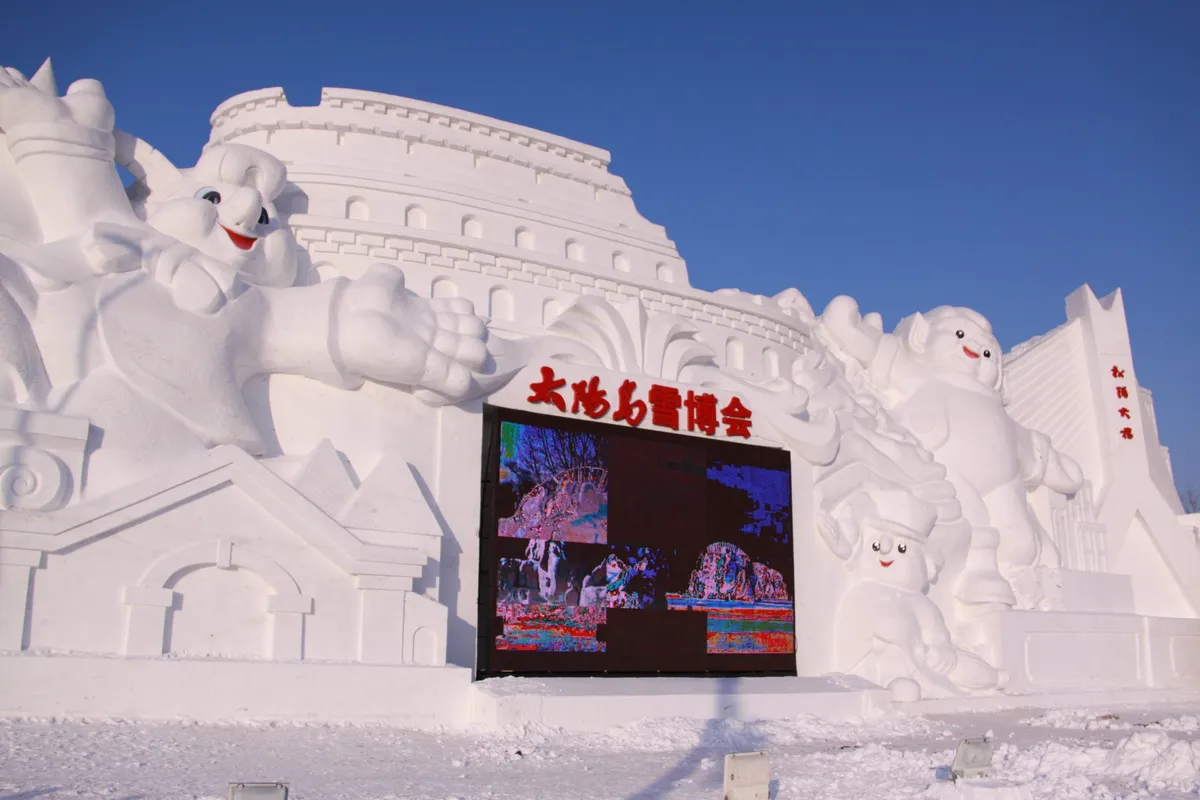A large snow sculpture archway with carved figures and Chinese characters reading Sun Island Snow Expo