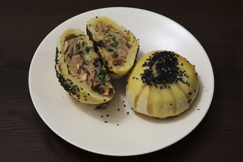 A halved sesame-topped Suzhou-style mooncake showing its flaky layers and minced pork filling