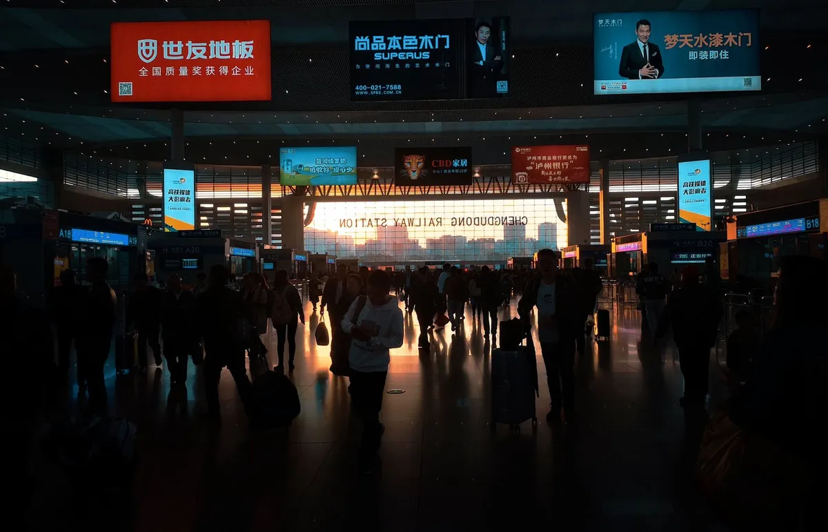 The crowded departure hall of Chengdu East railway station at dusk, with boarding gates and screens