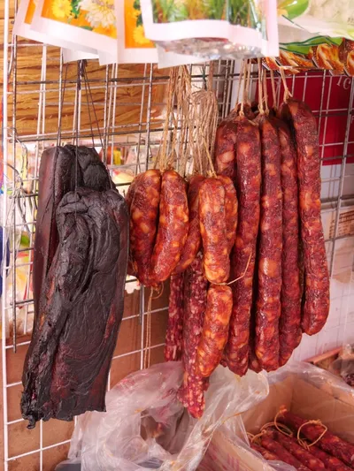 Dark, wood-smoked cured pork belly beside strings of Hunan-style sausages at a market stall