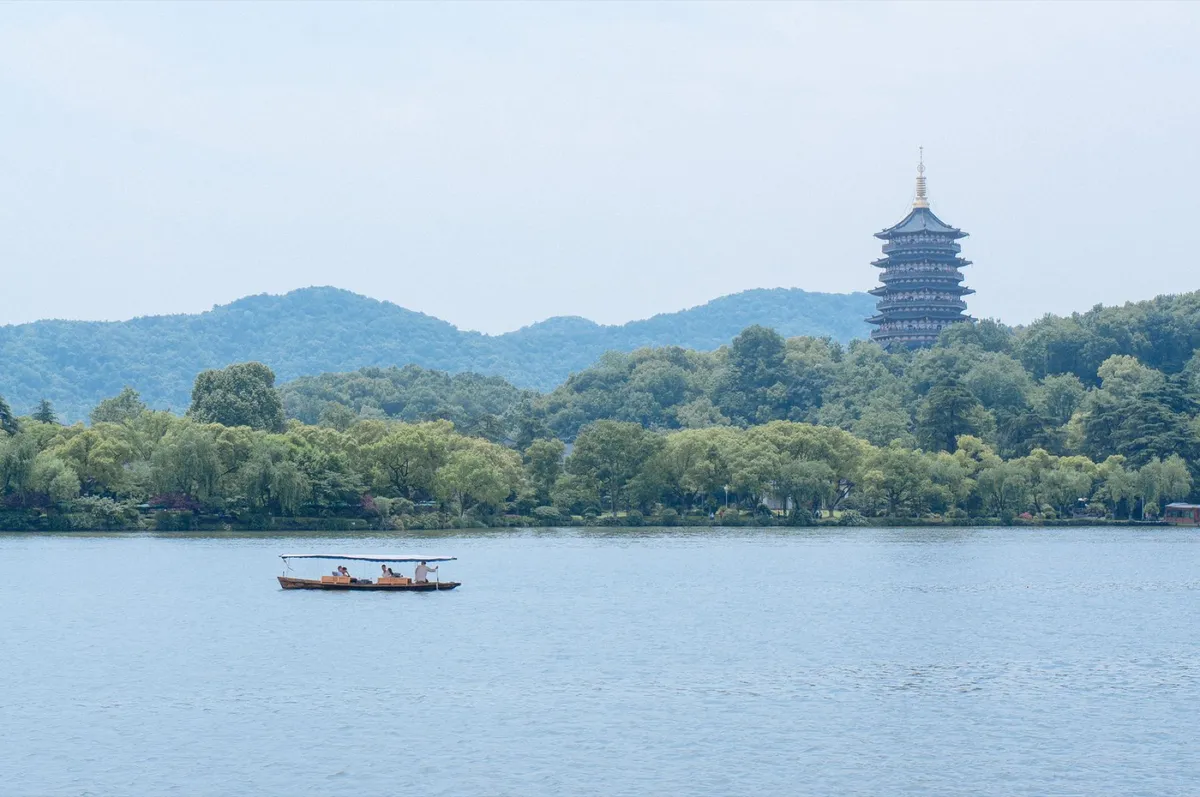 A traditional canopied boat crossing West Lake with Leifeng Pagoda visible on the shore