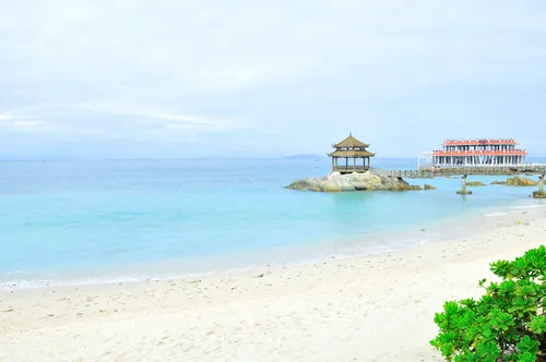 Clear turquoise water and white sand beach at Wuzhizhou Island, Sanya, with a pavilion on the rocks offshore