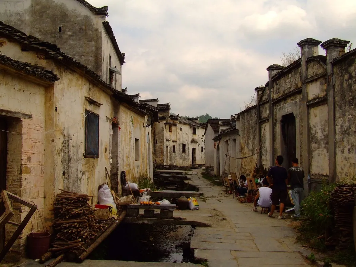 A stone lane between whitewashed Hui-style houses in Xidi village, with art students painting