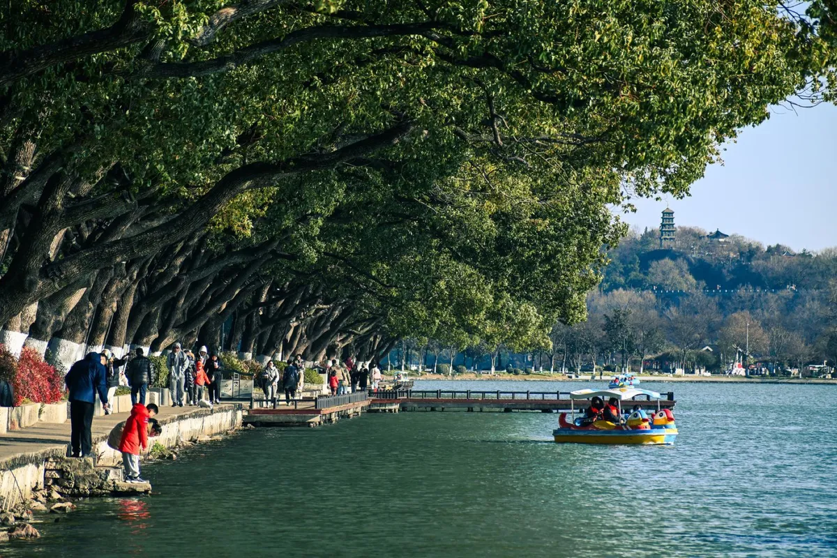 Pedal boats on Xuanwu Lake with a distant pagoda on a hill, lined by overhanging trees