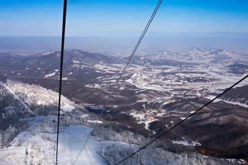 View from a chairlift over snow-covered slopes and forested mountains at Yabuli Ski Resort near Harbin