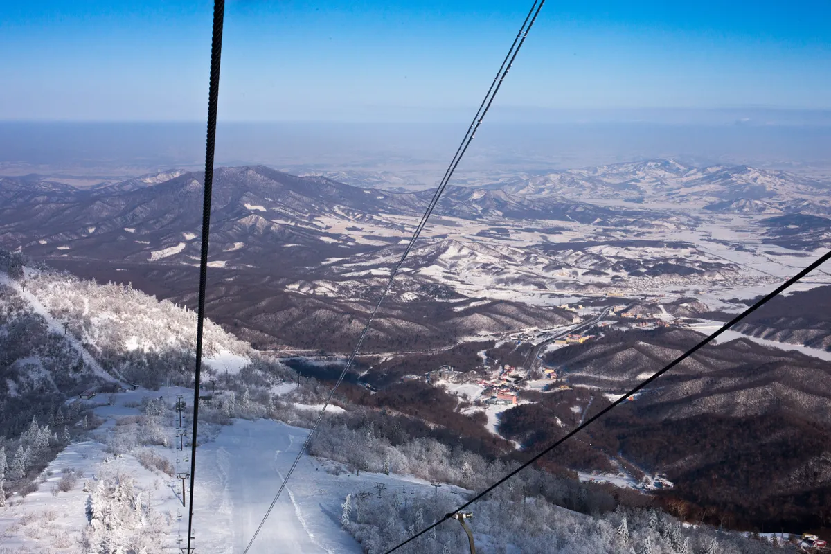 View from a chairlift over snow-covered slopes and forested mountains at Yabuli Ski Resort near Harbin
