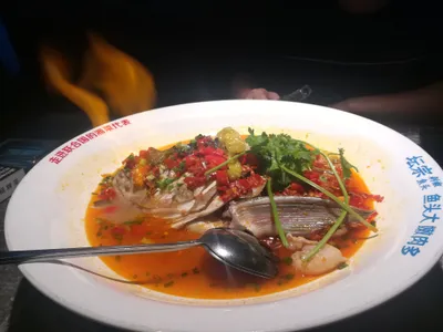 A whole steamed fish head topped with chopped red chilies, cilantro, and pickled peppers on a large plate