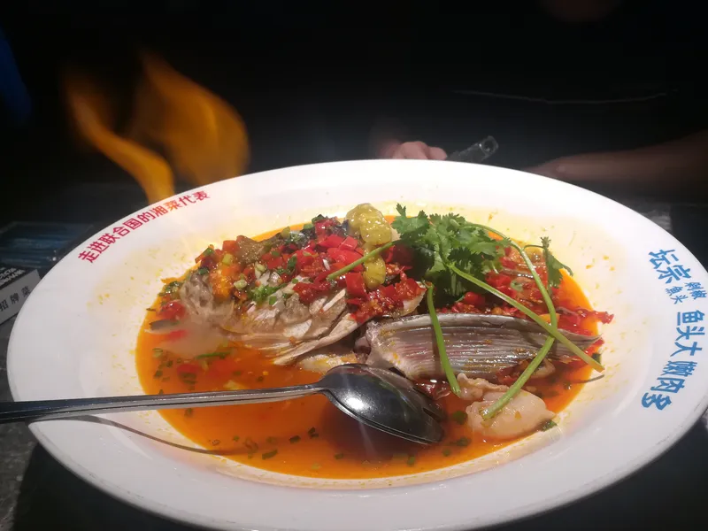 A whole steamed fish head topped with chopped red chilies, cilantro, and pickled peppers on a large plate